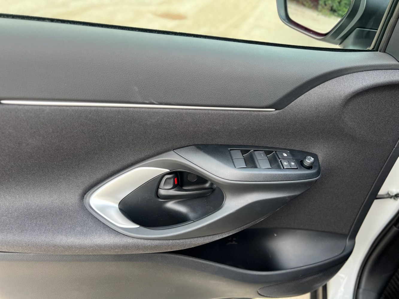 Interior door panel with handle, window controls, and mirror adjustment knob