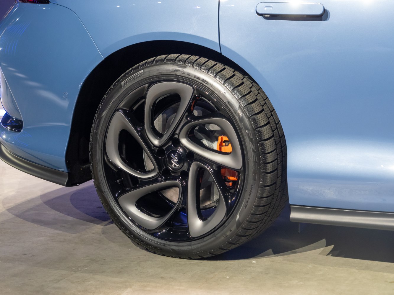 Modern black alloy wheel with orange brake caliper on a car.