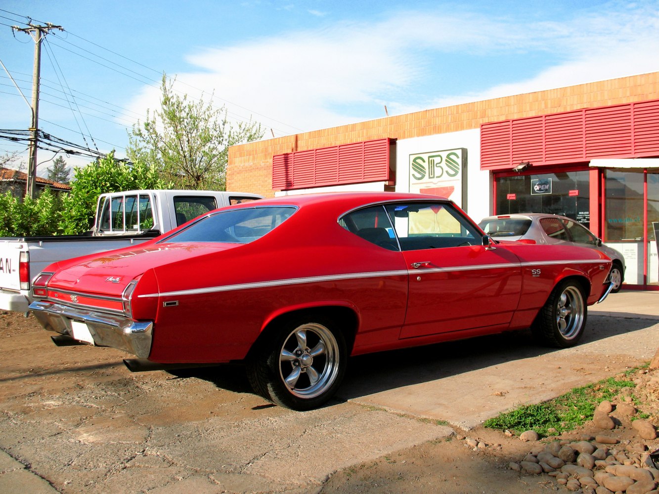 Red 1969 muscle car rear side view with chrome wheels and SS badge