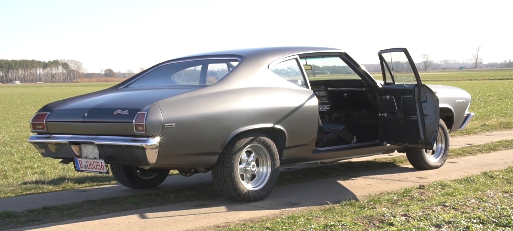 Rear-side view of a classic muscle coupe with open driver door and sporty wheels