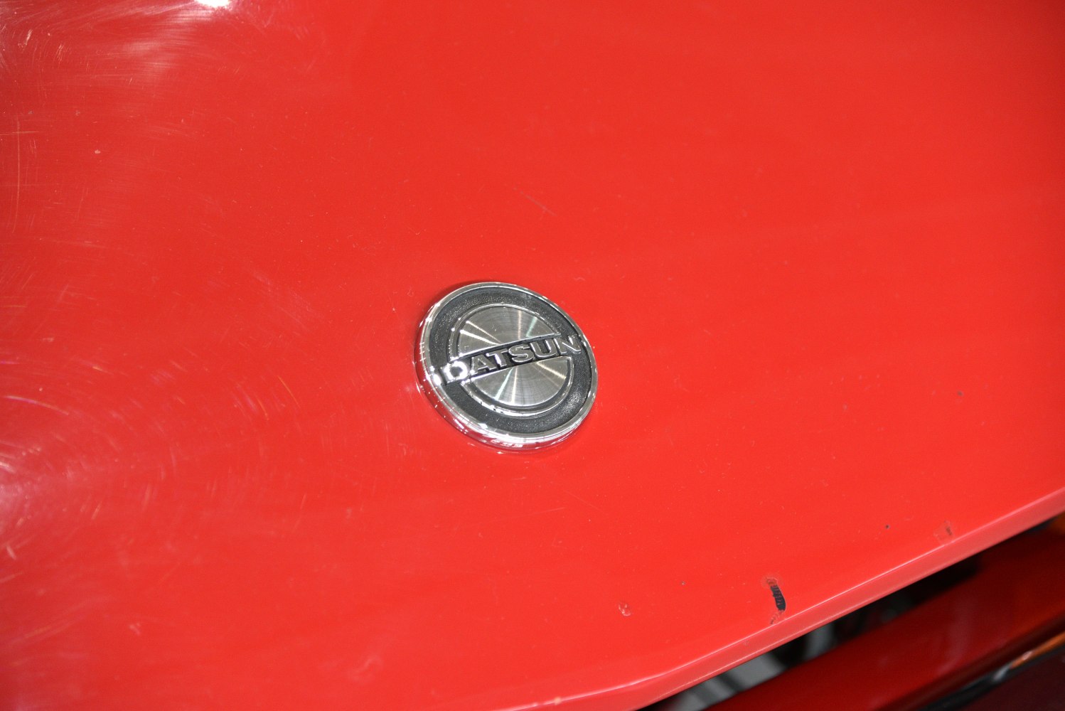 Close-up of Datsun front badge on red car hood