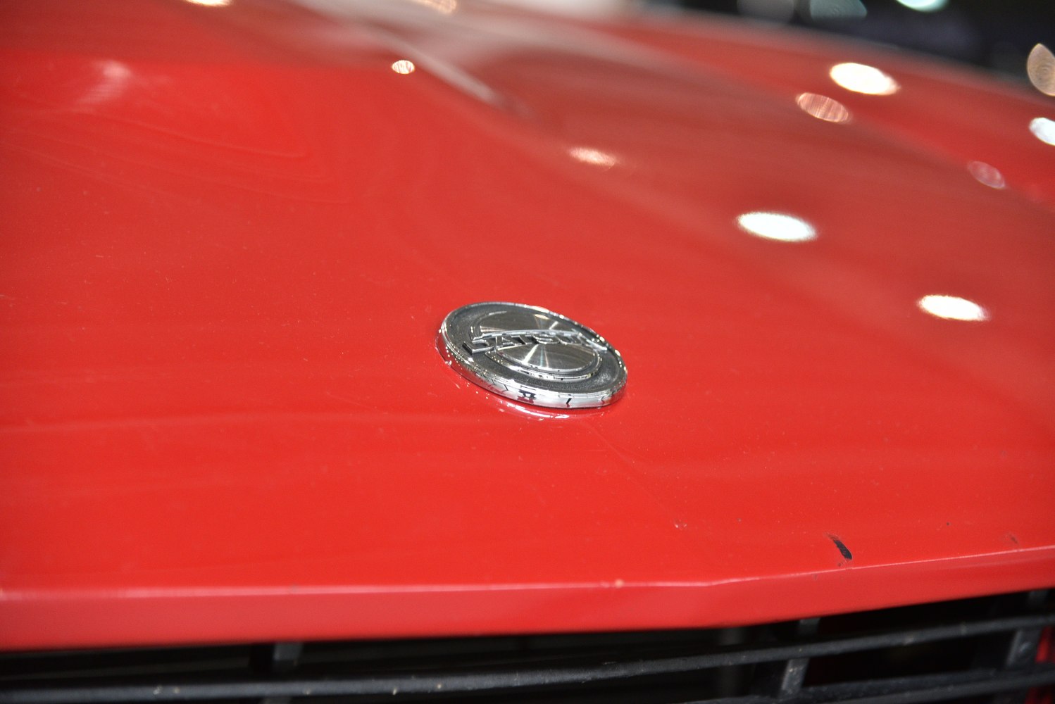 Close-up of a vintage car hood emblem on bright red surface