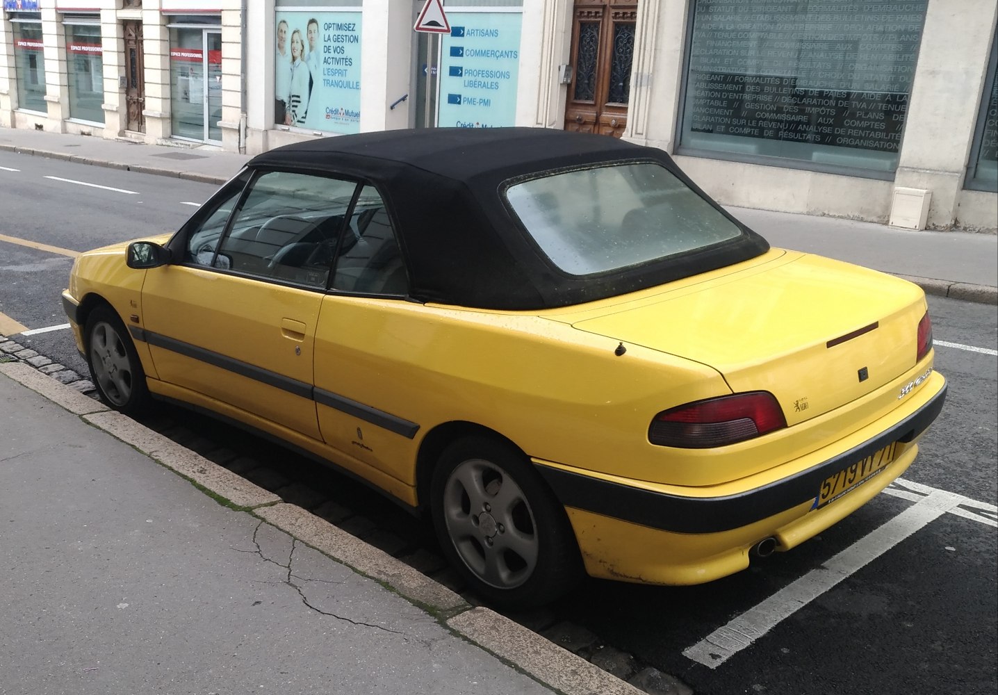 Yellow convertible with black soft top parked on city street