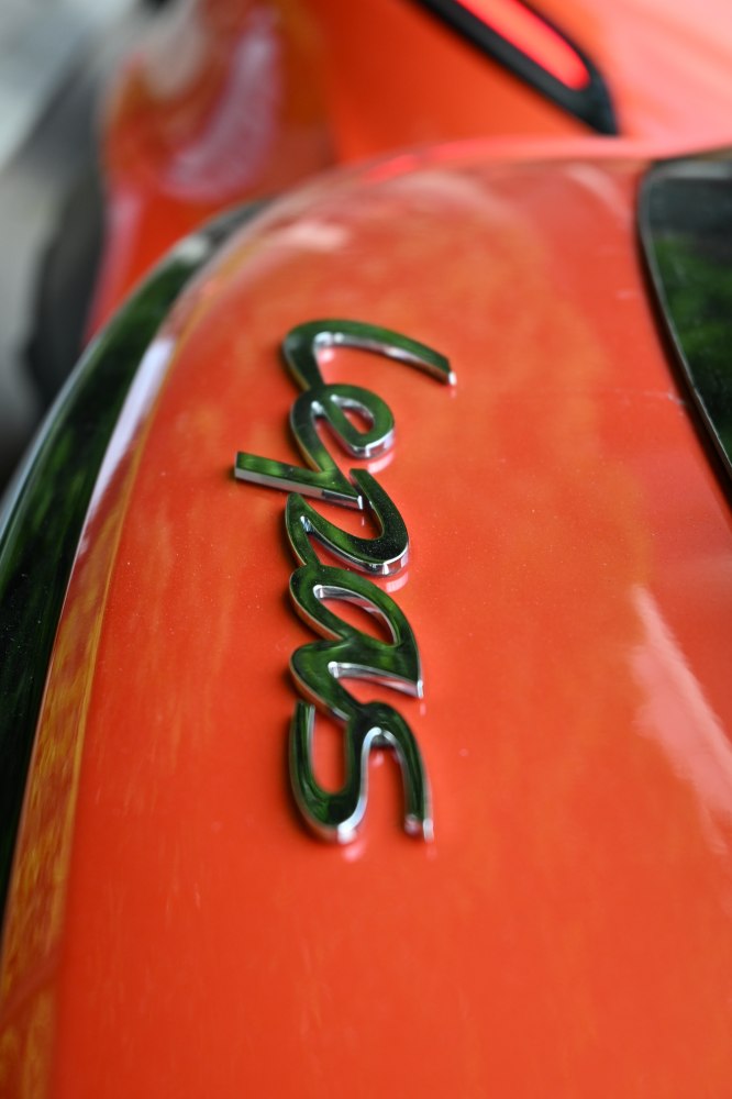 Close-up of shiny chrome Lepas badge on orange vehicle