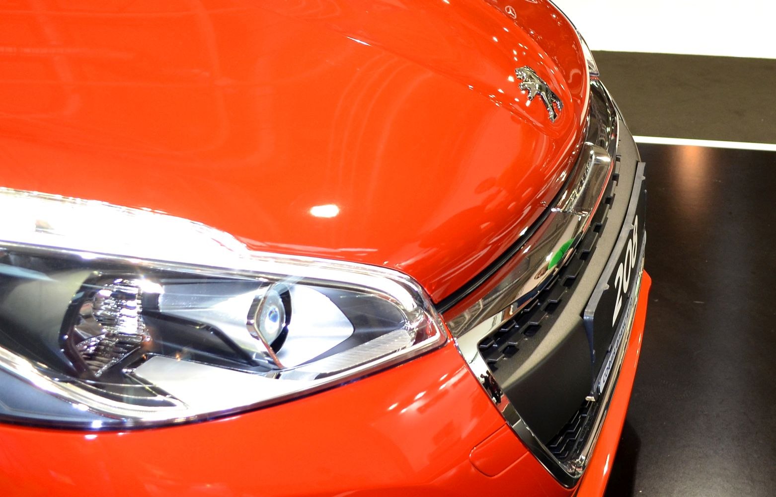 Close-up of headlight and front grille with emblem on orange surface