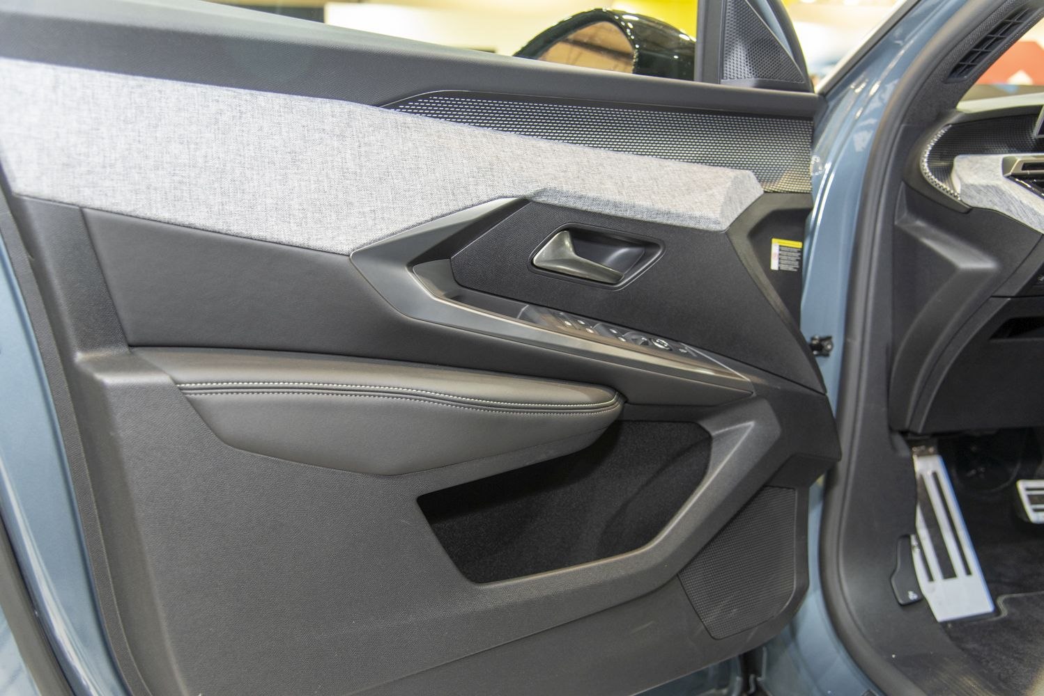 Car door interior with fabric trim, leather armrest, and control buttons