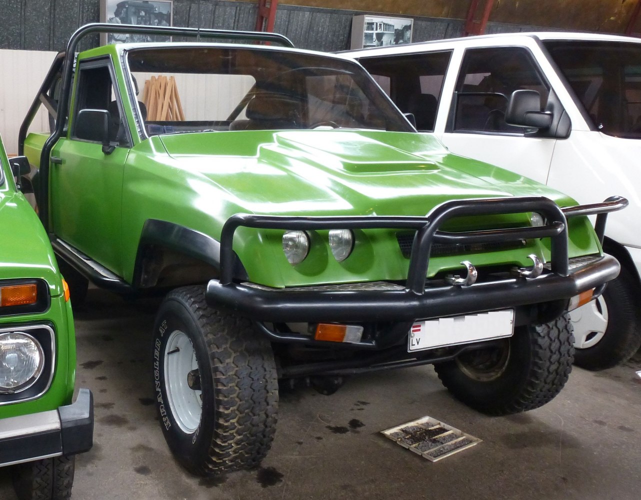 Green off-road pickup with raised hood and front bull bar