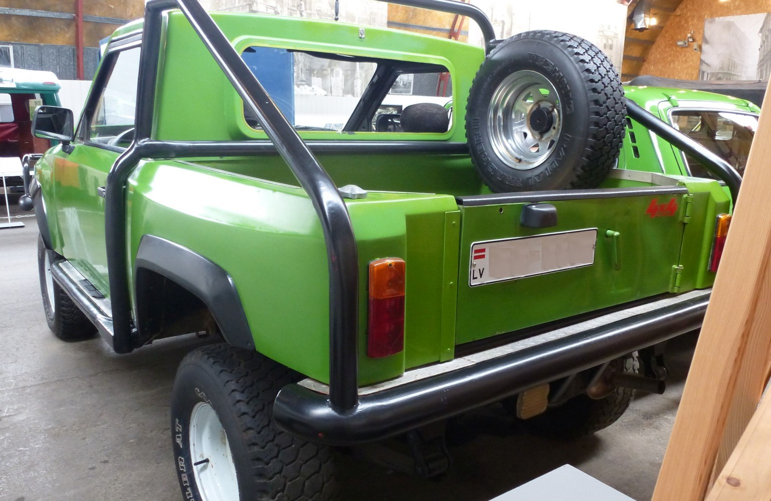 Green pickup with rear roll cage and mounted spare tire