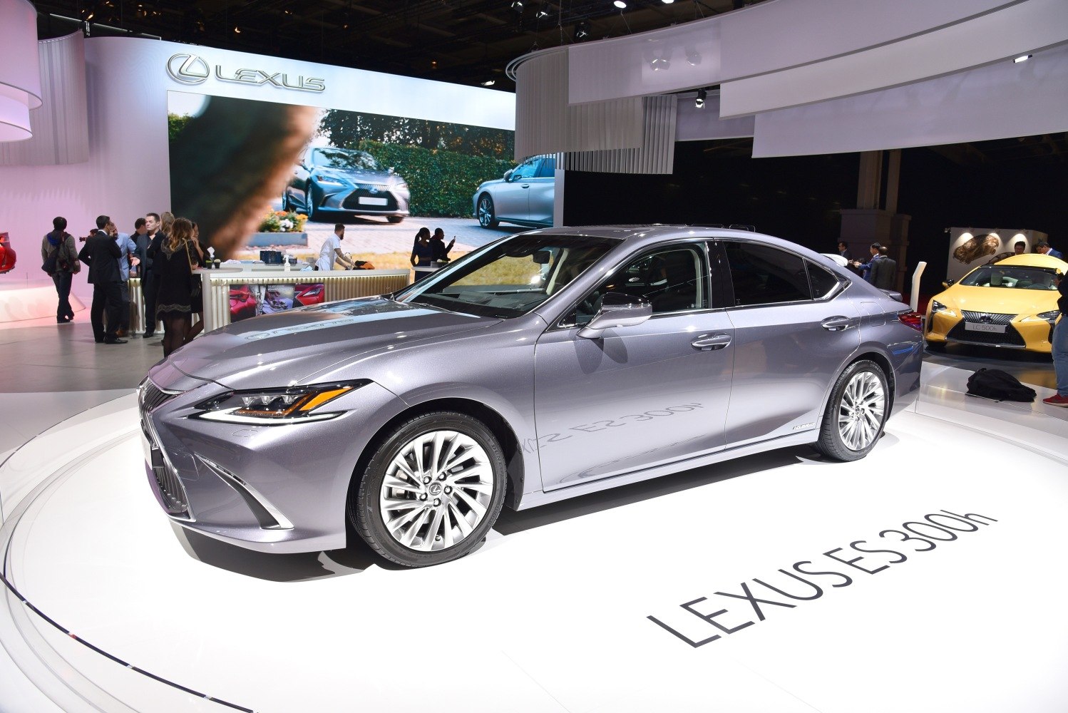 Sleek silver hybrid sedan with sharp headlights and multi-spoke wheels on show platform
