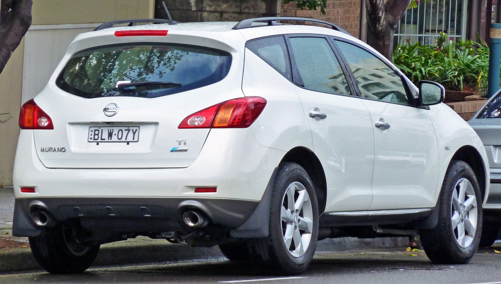 Rear view of white SUV with dual exhaust, taillights, roof rails, and rear window wiper