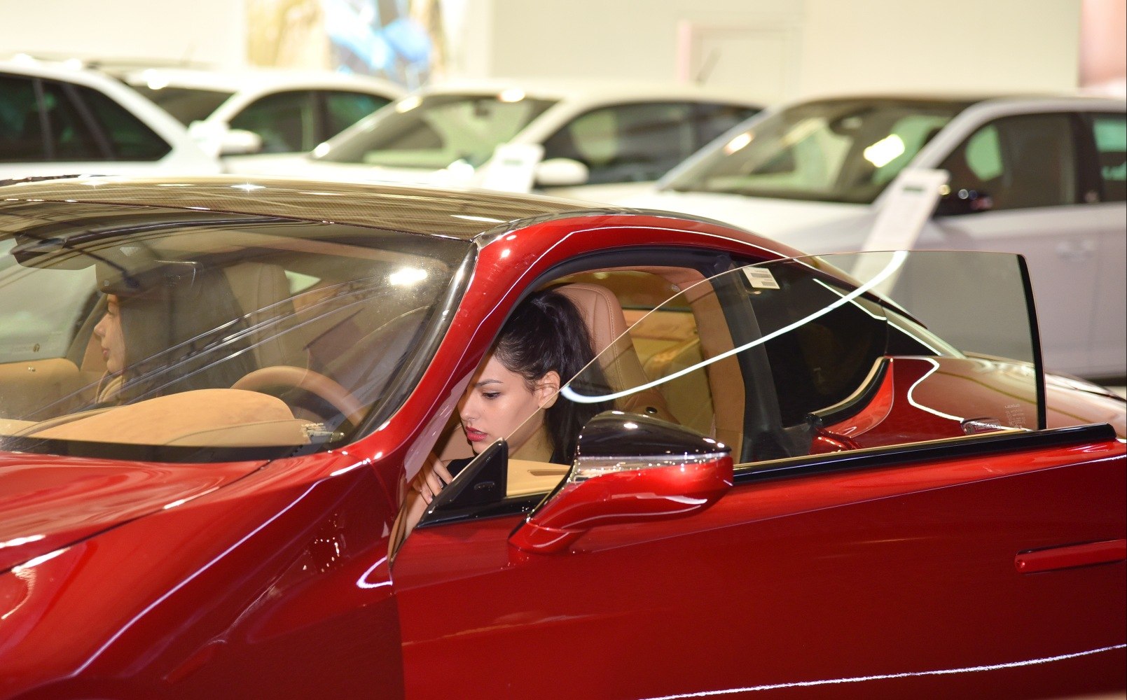 Open door view of sporty coupe interior with beige seats and woman inside
