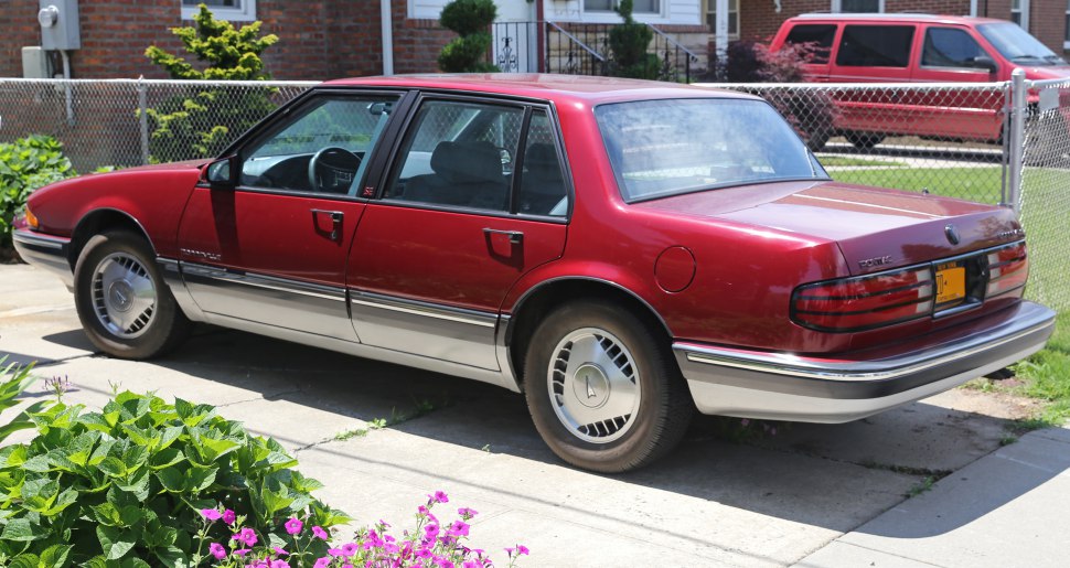 Rear-side view of red two-tone 1987 sedan with hubcap wheels