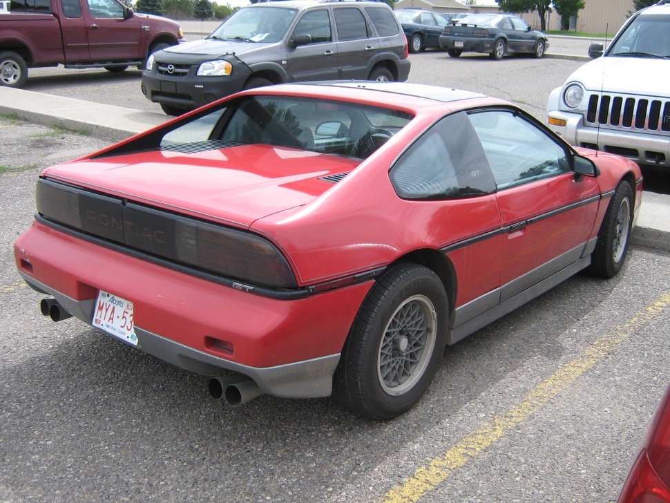 Red sports coupe with mid-engine layout, dual exhaust, and alloy wheels from rear-side view