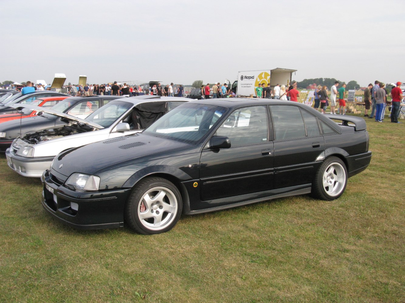 Black sedan with rear spoiler and five-spoke alloy wheels.