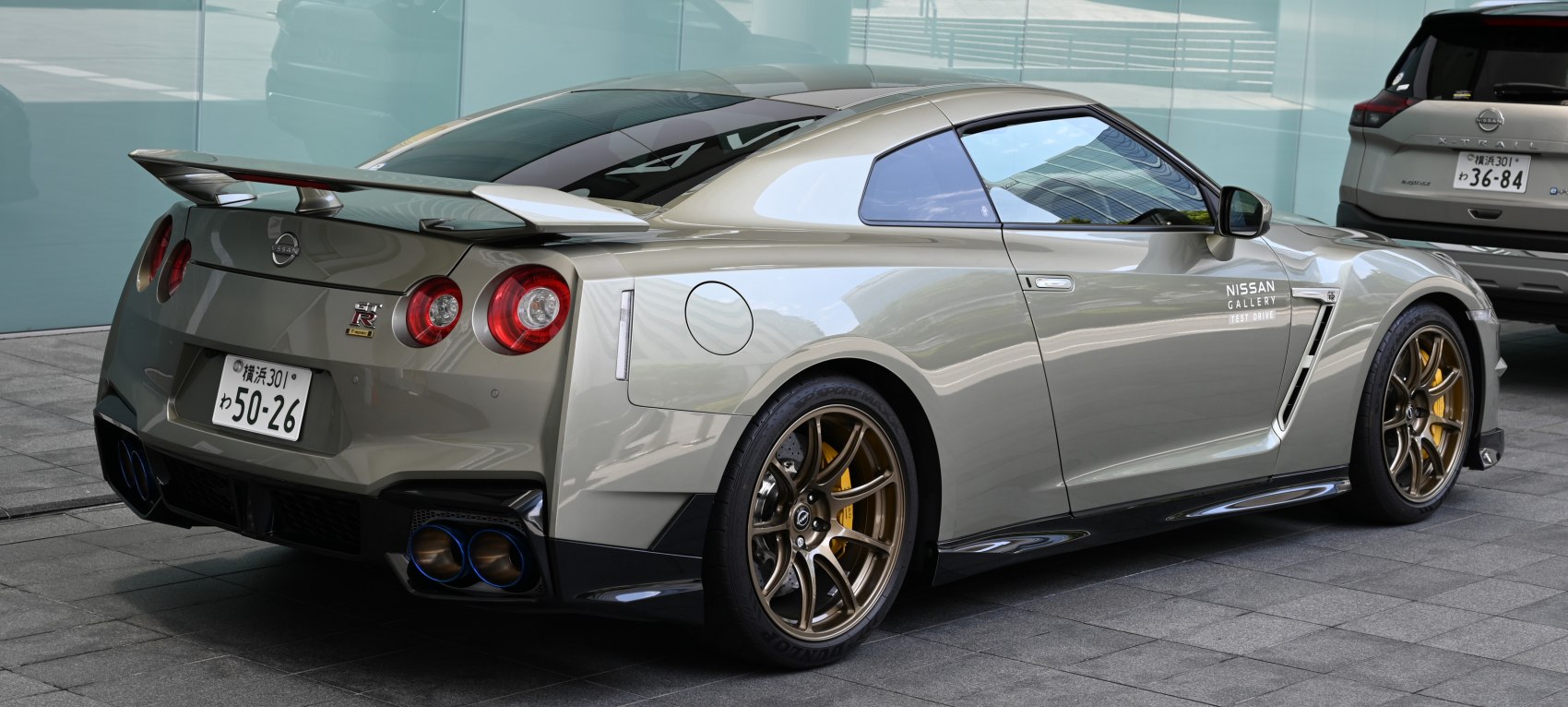 Rear and side view of a modern sports coupe with quad exhaust and bronze wheels