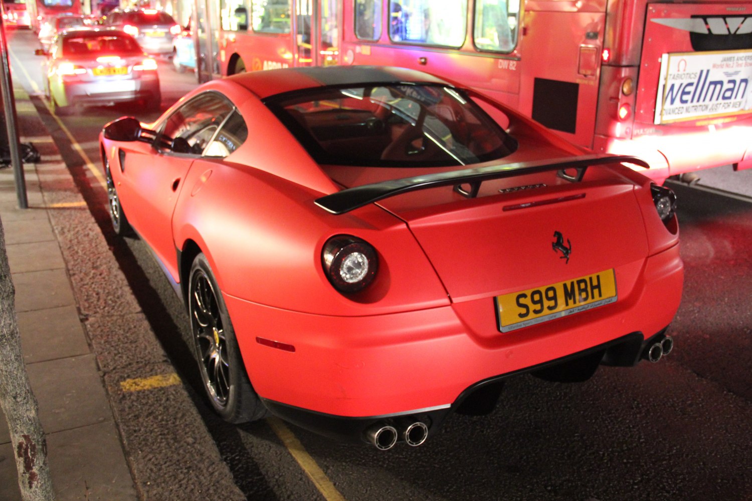 Matte red sports car rear with black spoiler and quad exhausts