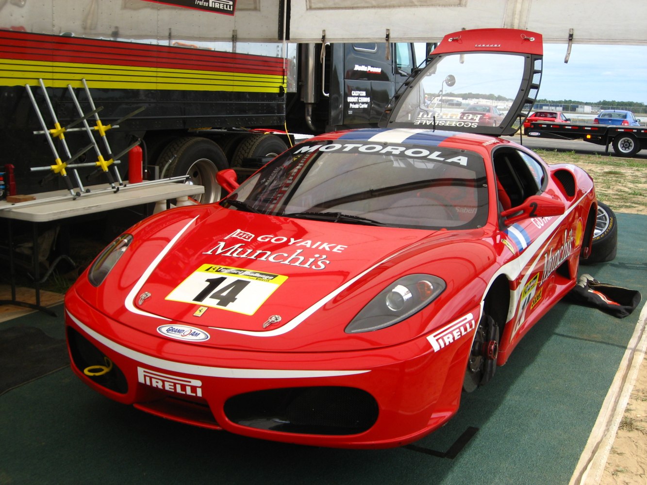Red racing car with gullwing door and multiple sponsor decals.