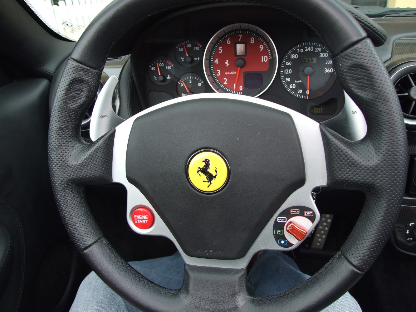 Steering wheel with Ferrari emblem, engine start button, and dashboard gauges.