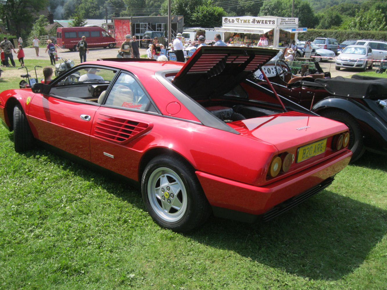 Red sports coupe with rear engine hood open, side air vents, and classic wheels.