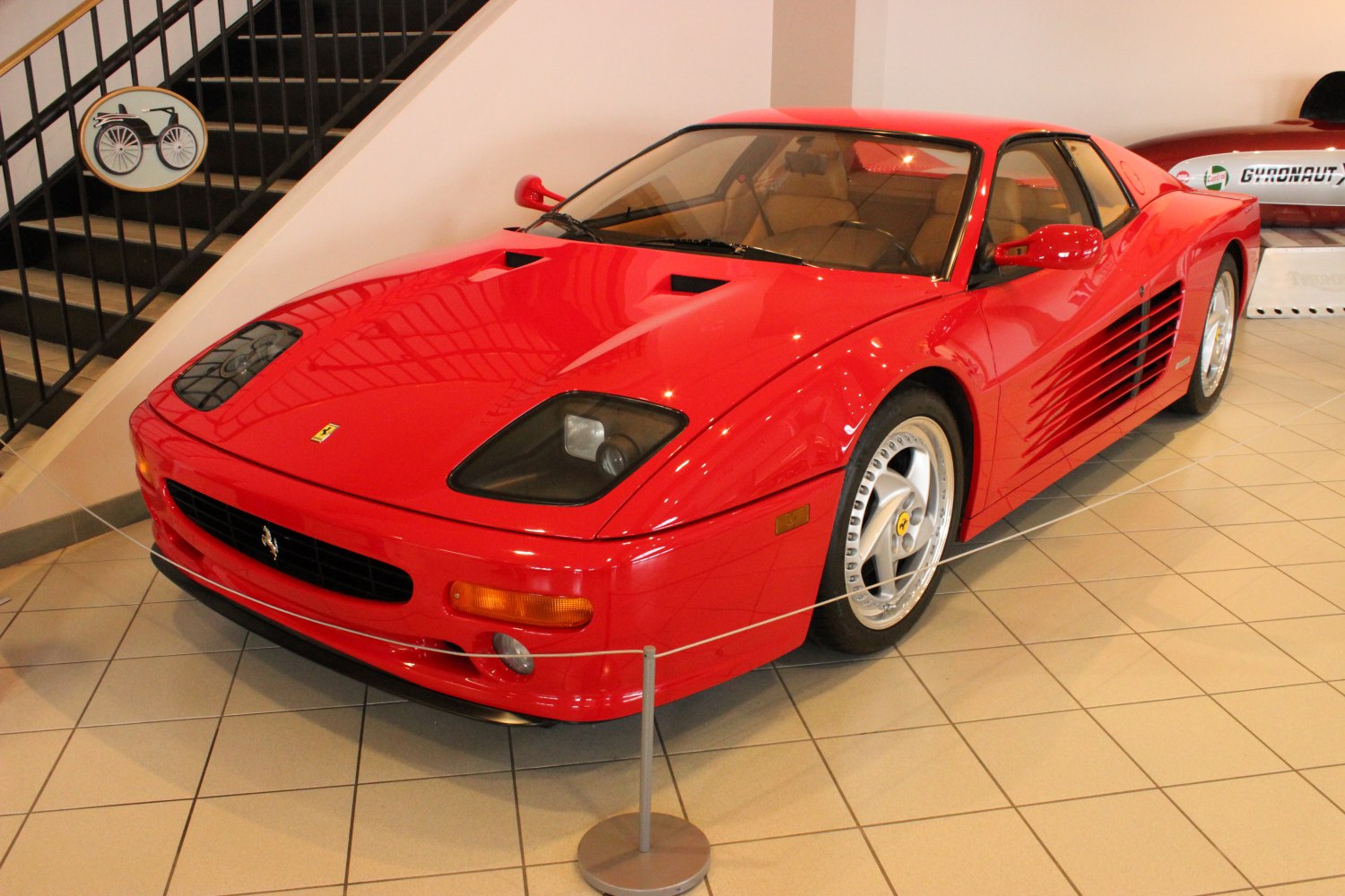 Front side view of a red sports coupe with distinctive side air intakes.