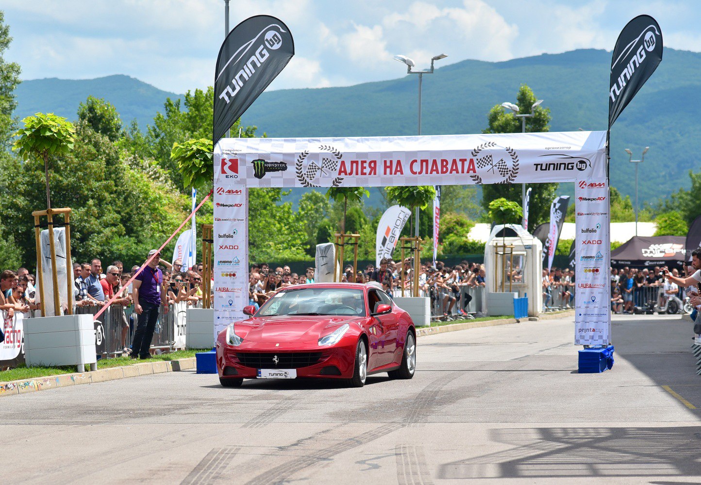 Red sports coupe crossing finish line with crowd and banners