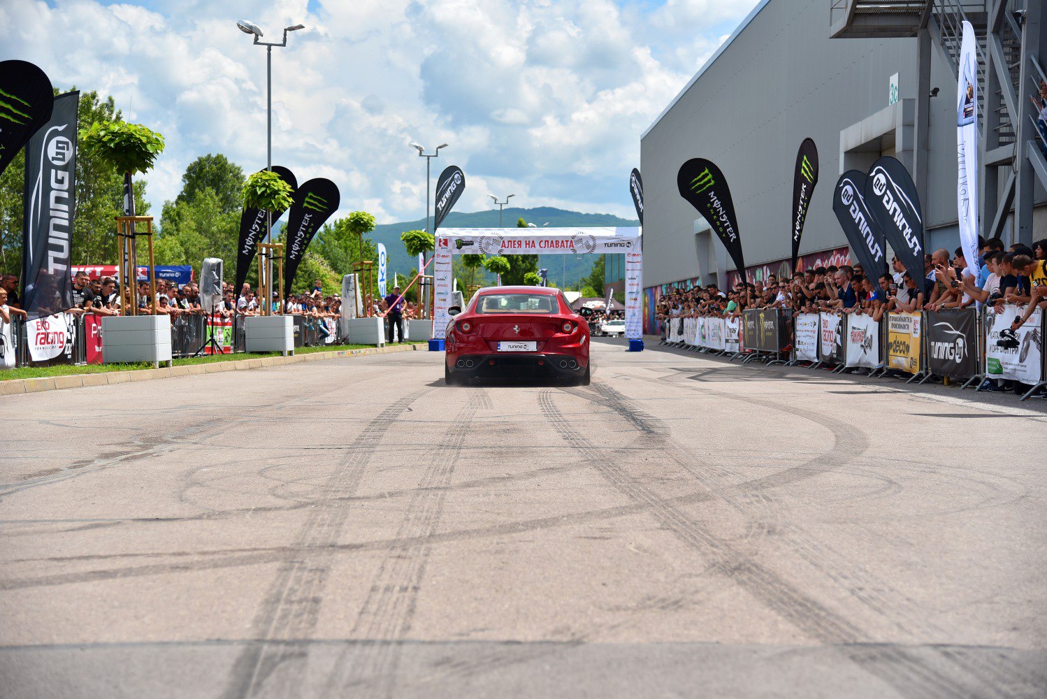 Rear view of red sports car performing burnout on event road.