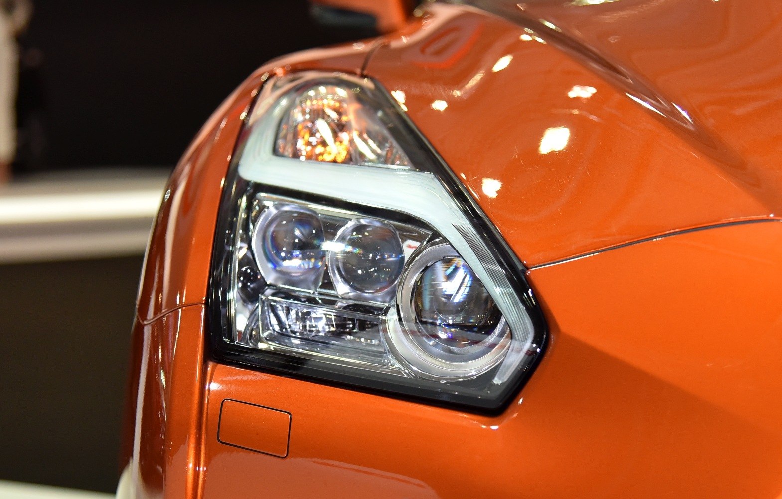 Close-up of LED headlight with detailed lenses and orange body paint