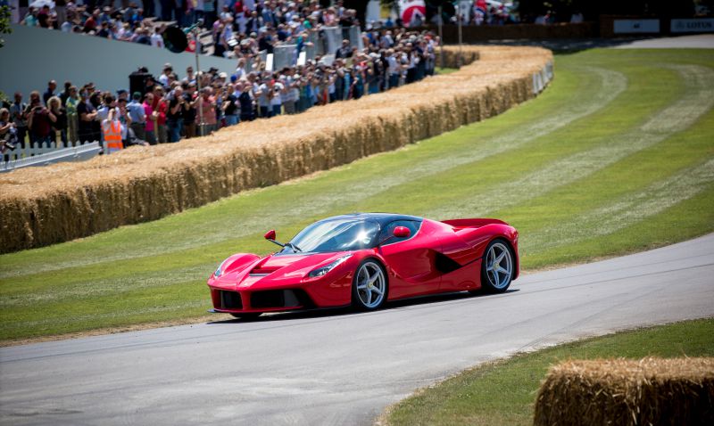 Red sports coupe on road at car event with crowd and hay bale barriers