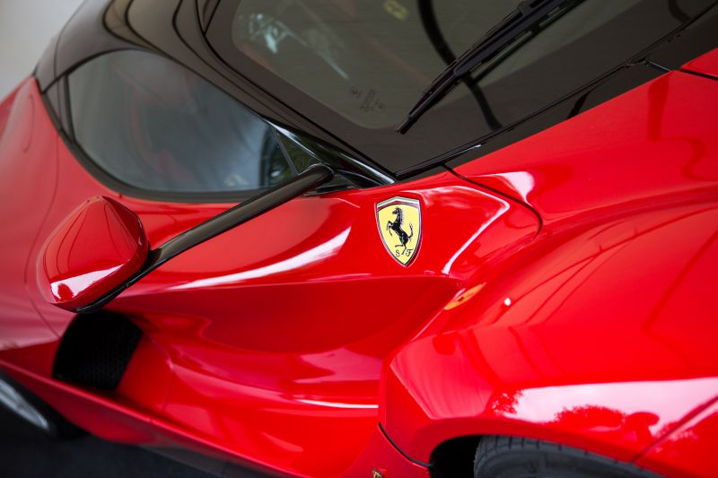 Close-up of a car side with emblem, side mirror, and aerodynamic body in red.