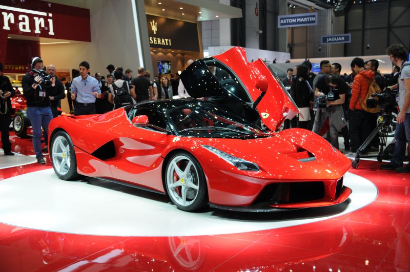 Sleek red sports car with open upward-swinging doors on display platform