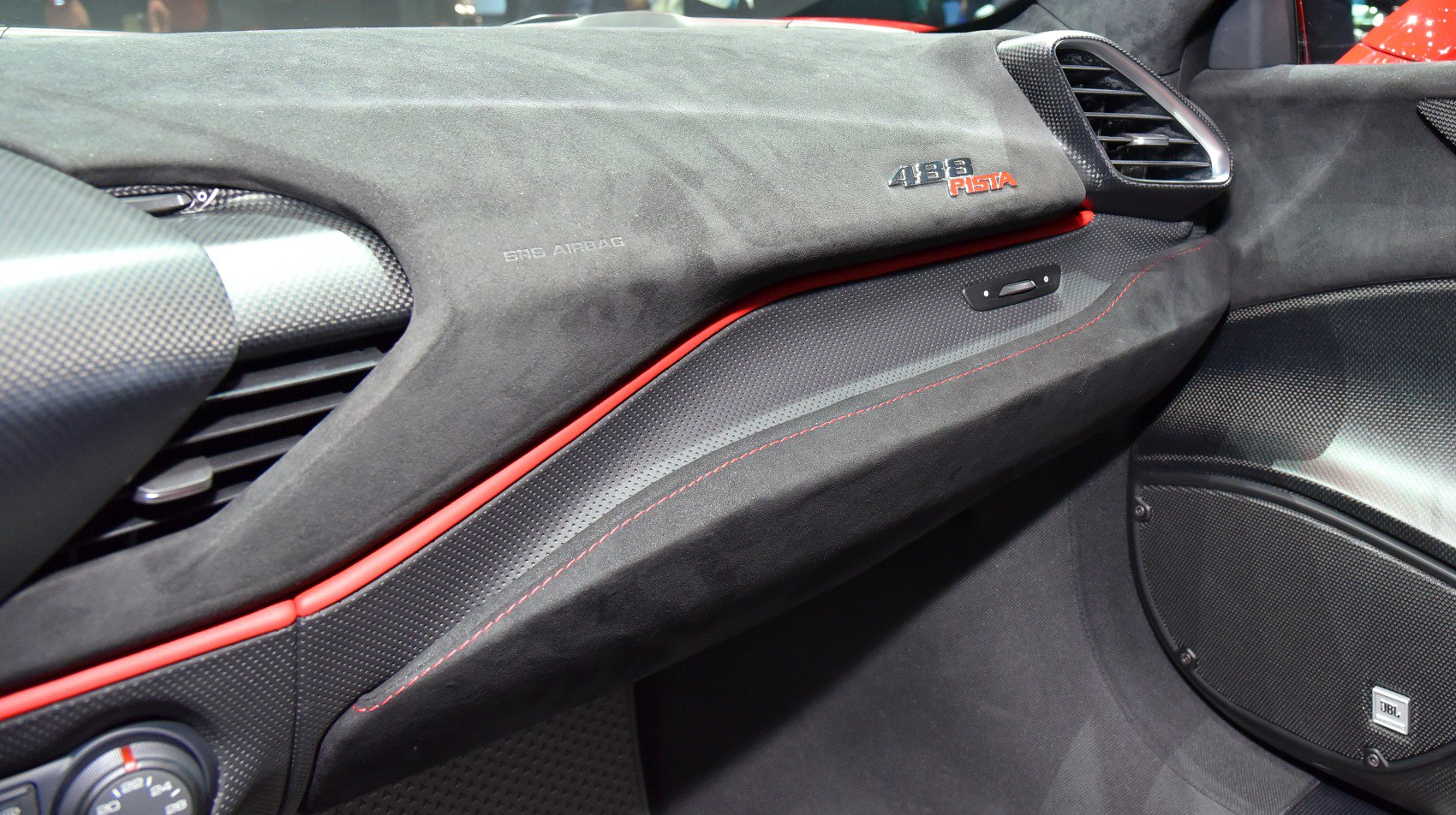 Close-up of luxury car dashboard with carbon fiber, Alcantara, and red stitching.