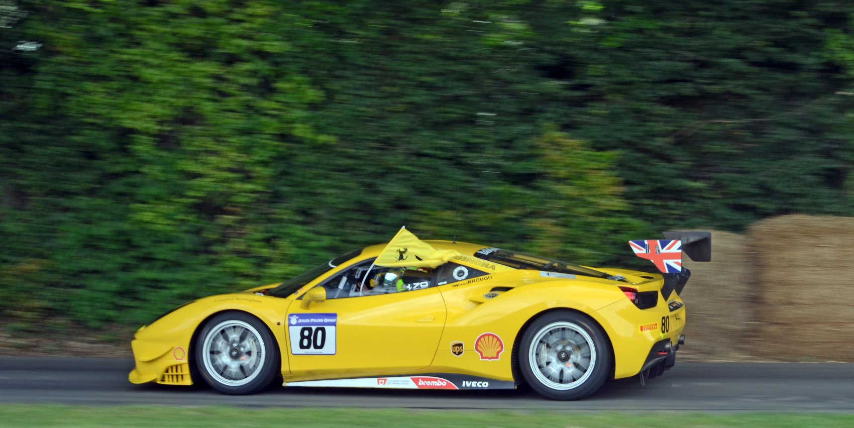 Yellow 2016 Ferrari 488 Challenge racing car in side profile with British flag on rear wing.