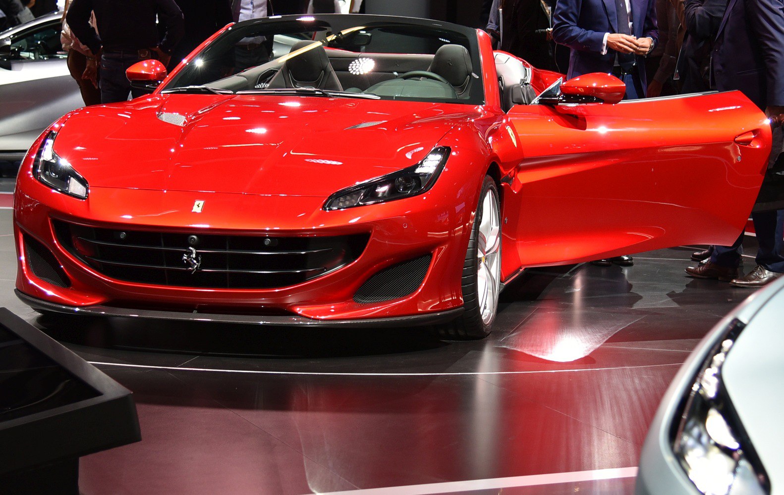 Front view of a sleek convertible with open driver door under showroom lights