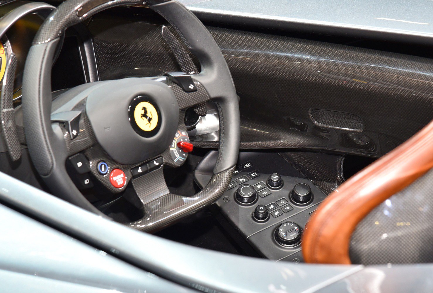 Carbon fiber sports steering wheel and control panel with multiple buttons and dials.