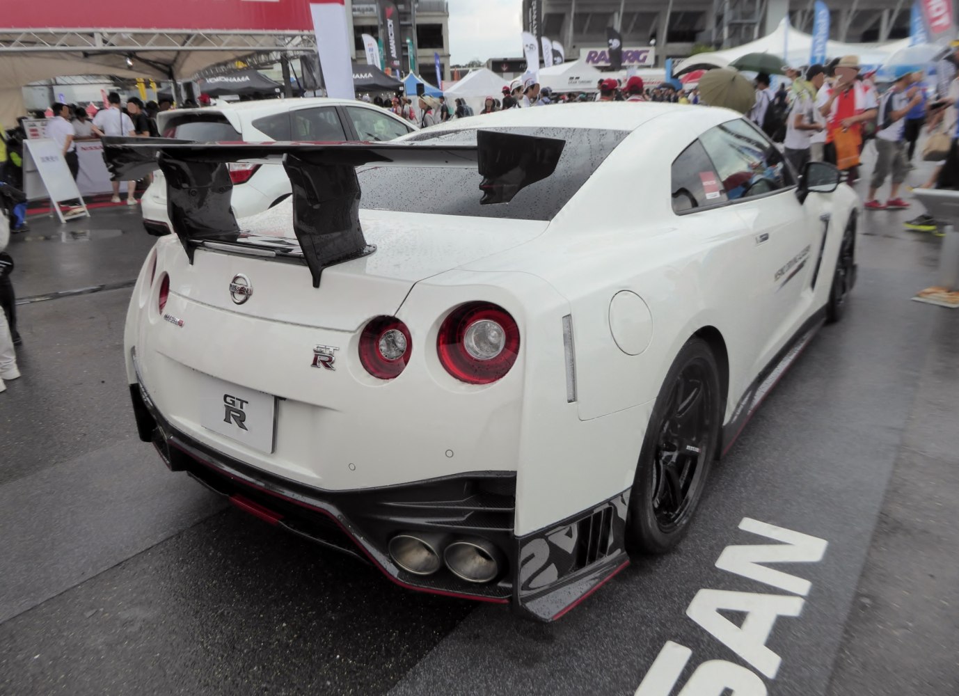 Rear view of sports car with large racing rear wing and quad exhaust.
