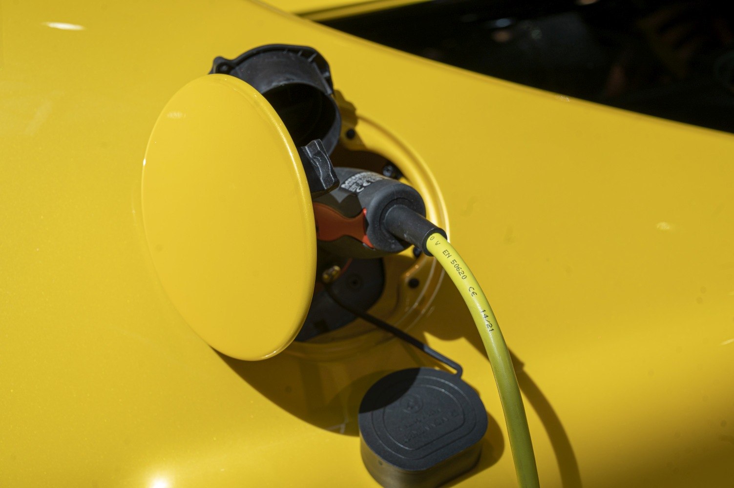 Electric charging port with plug and cable on yellow vehicle body