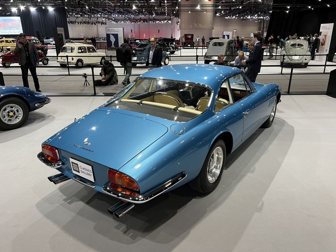 Rear view of vintage blue sports coupe with chrome dual exhausts and beige interior.