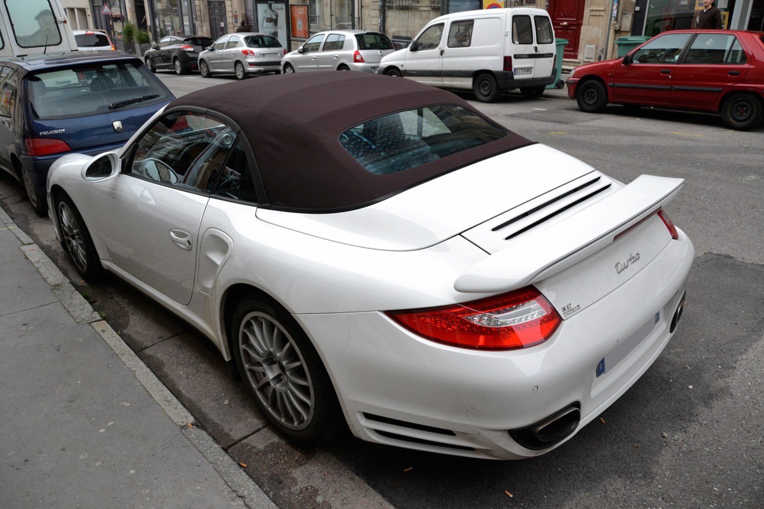 White convertible Porsche 911 Cabriolet with soft top, rear spoiler, and twin exhausts