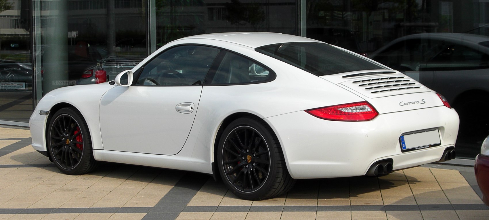 Rear three-quarter view of white sports coupe with black rims and dual exhaust