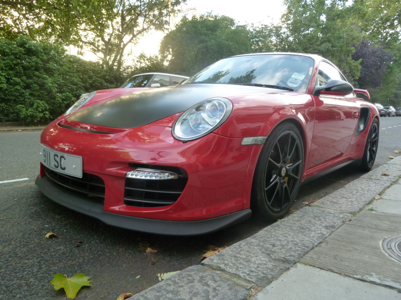 Red sports car with black hood and black sport rims, side front perspective.
