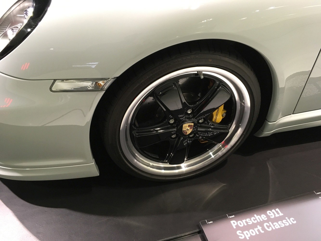 Close-up of black alloy wheel with yellow brake caliper and front fender indicator.