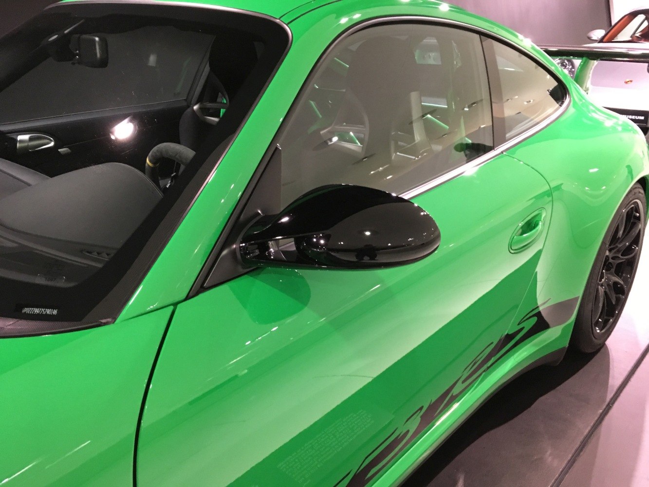 Glossy black side mirror with door and racing decal on vibrant green sports coupe