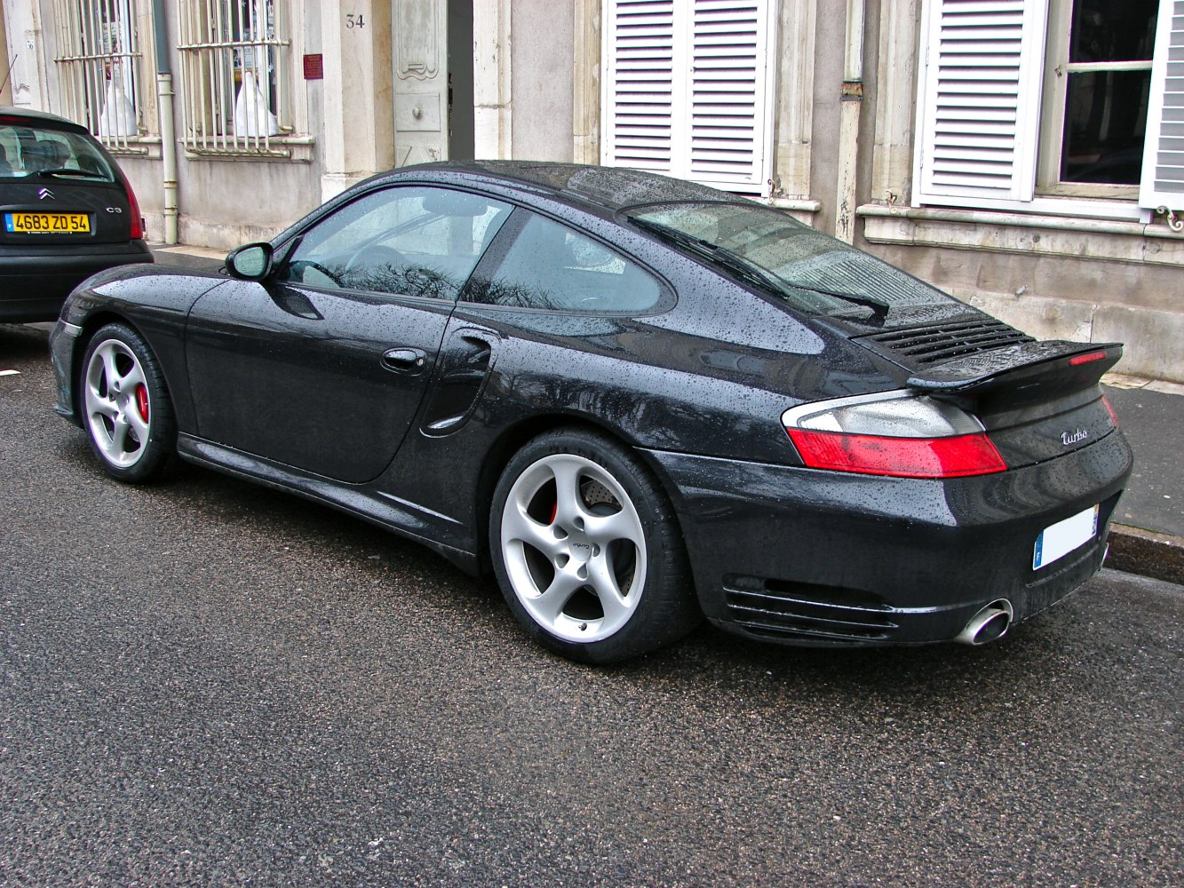 Rear side view of a black sports coupe with raised rear spoiler and five-spoke alloy wheels.