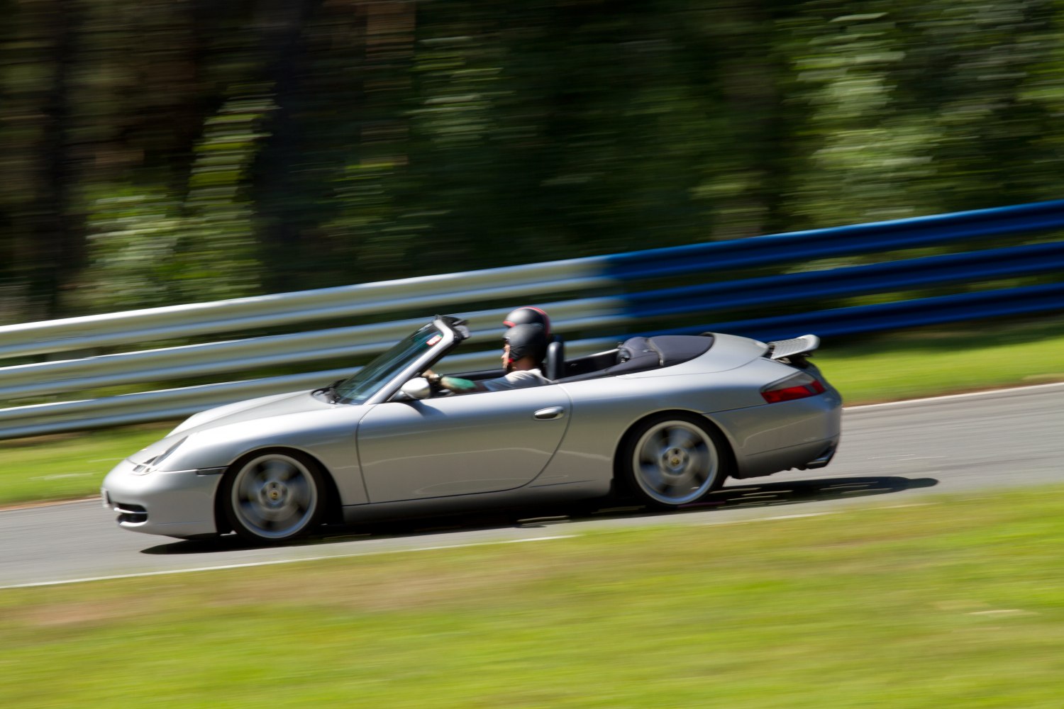 Silver convertible sports car in motion on a race track with driver wearing helmet
