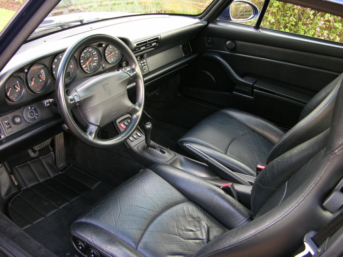 Classic 1990s car interior with black leather seats and analog dashboard