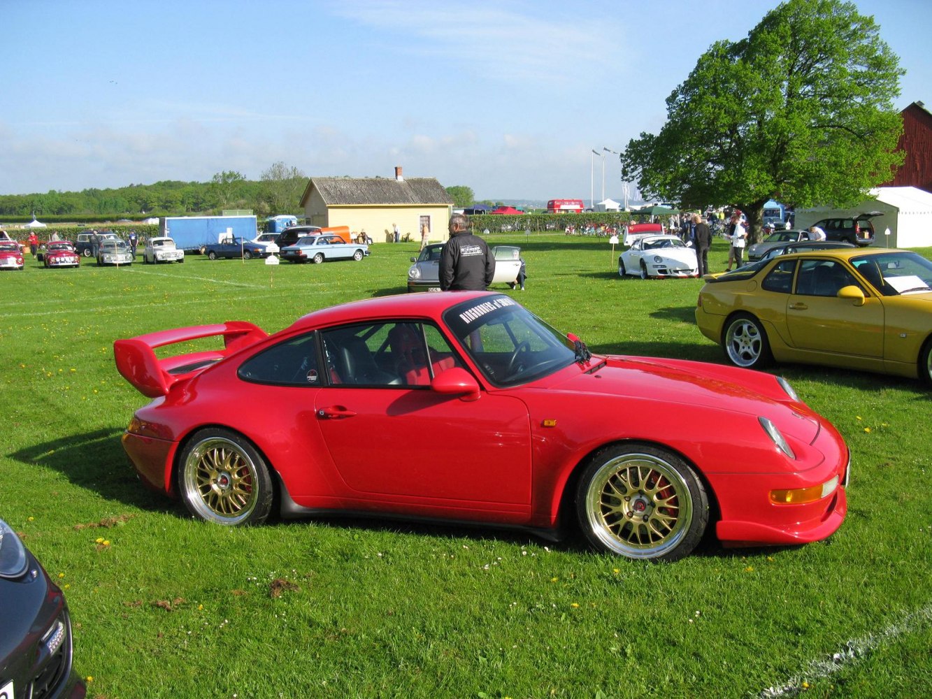 Red sports coupe side view with gold multi-spoke wheels and rear wing spoiler