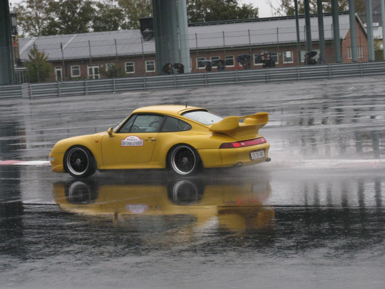 Yellow coupe with large rear wing driving on wet racing track