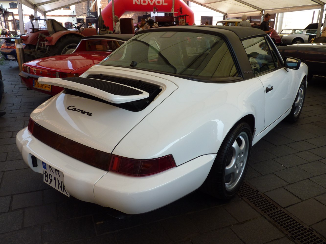 White vintage Porsche 911 Targa with rear spoiler and soft top roof.