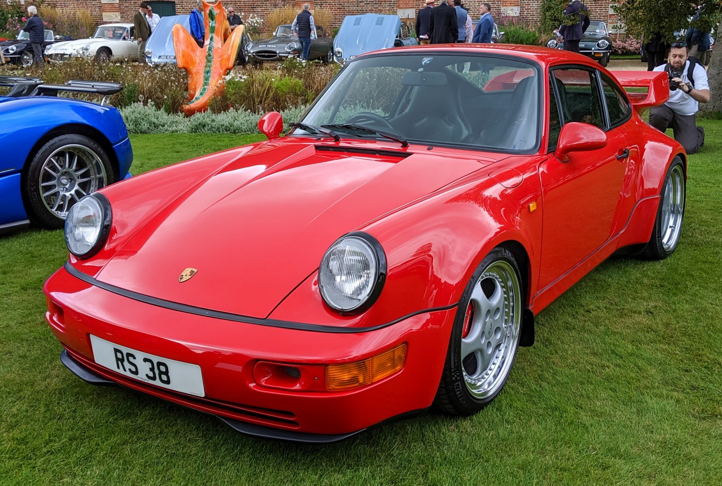 Red sports coupe with wide fenders and large rear wing on grass