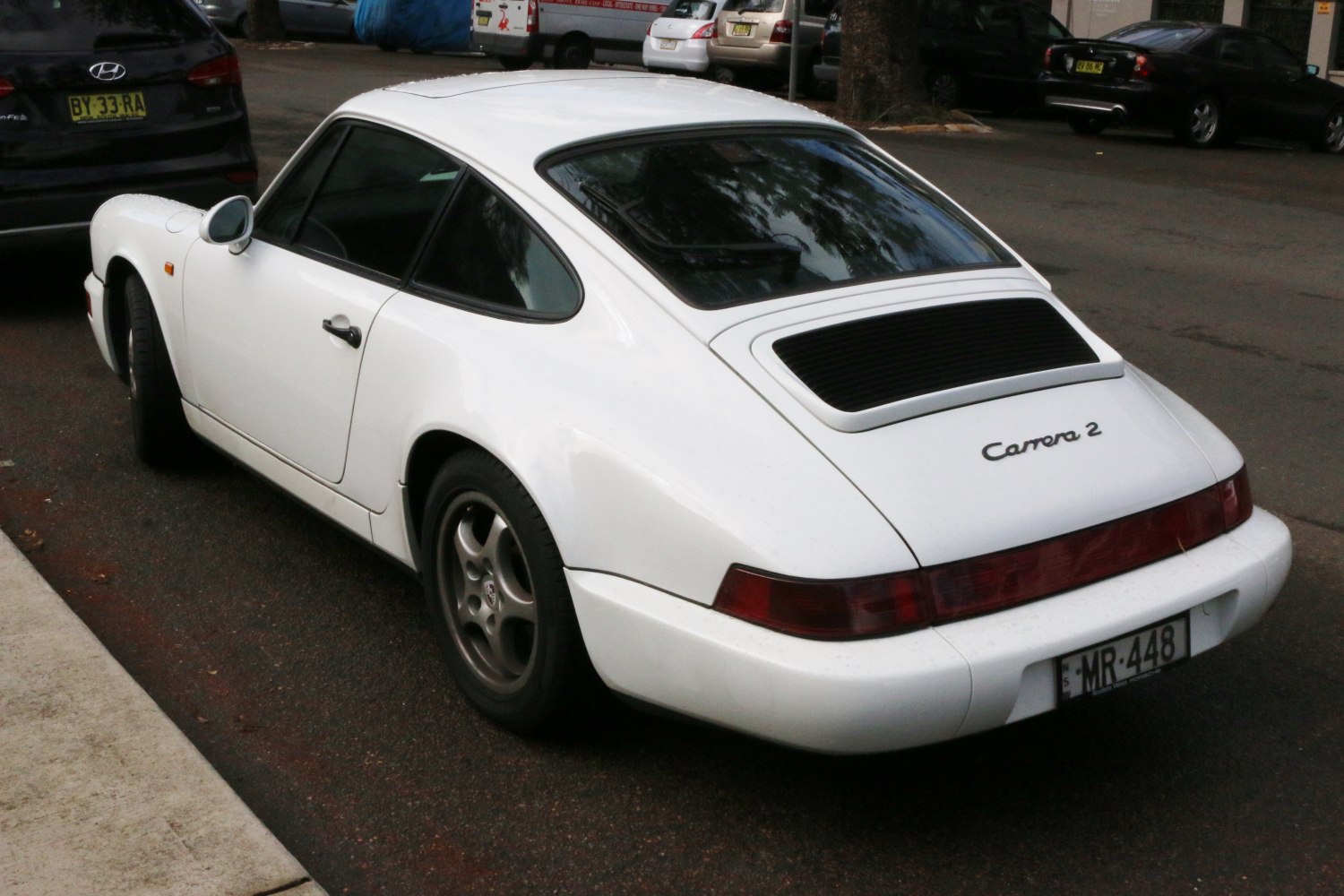 Rear side profile of a classic 1990s sports coupe with distinctive sloping roof and wide rear fenders.